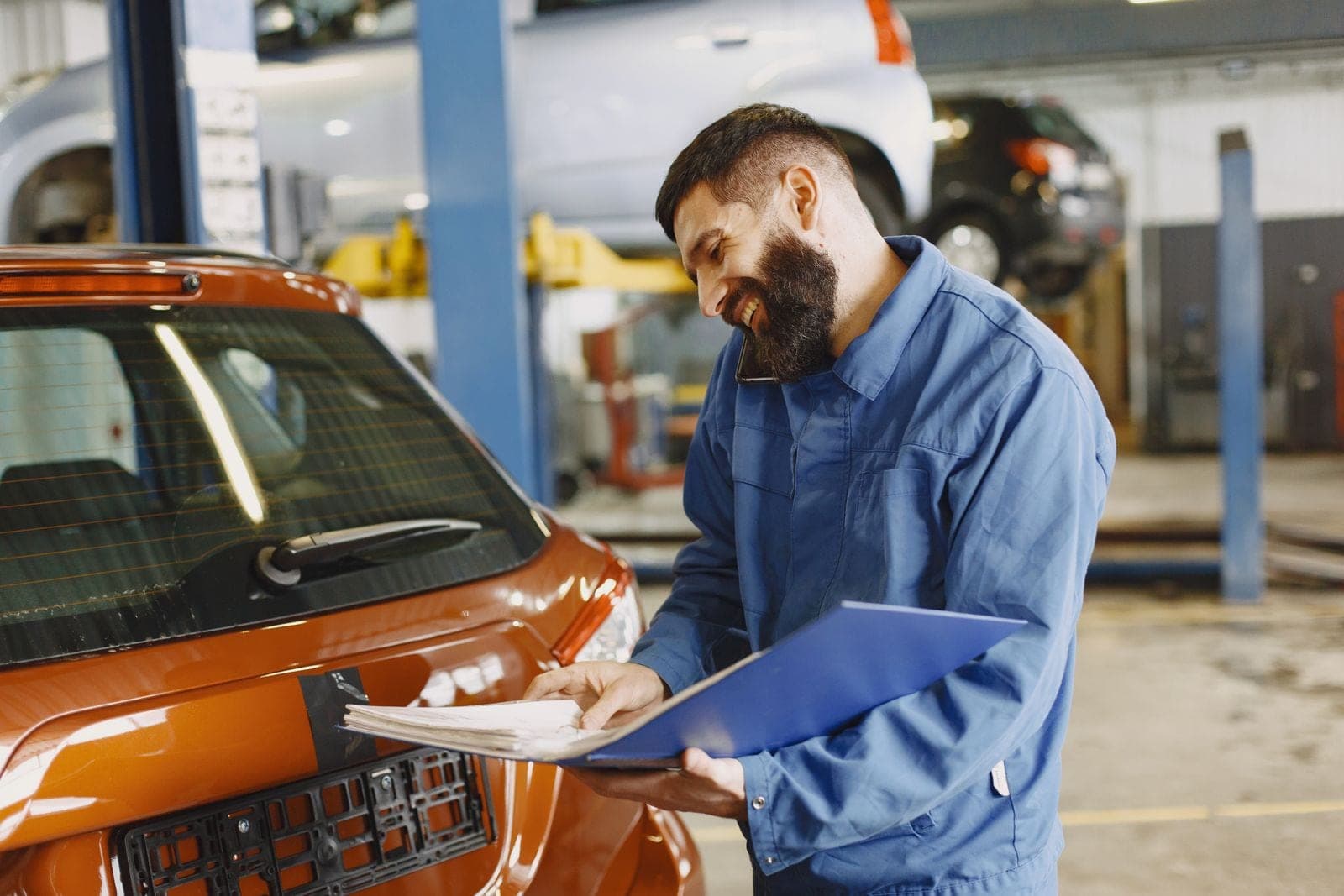 Technician reviewing paperwork beside an orange car in the shop