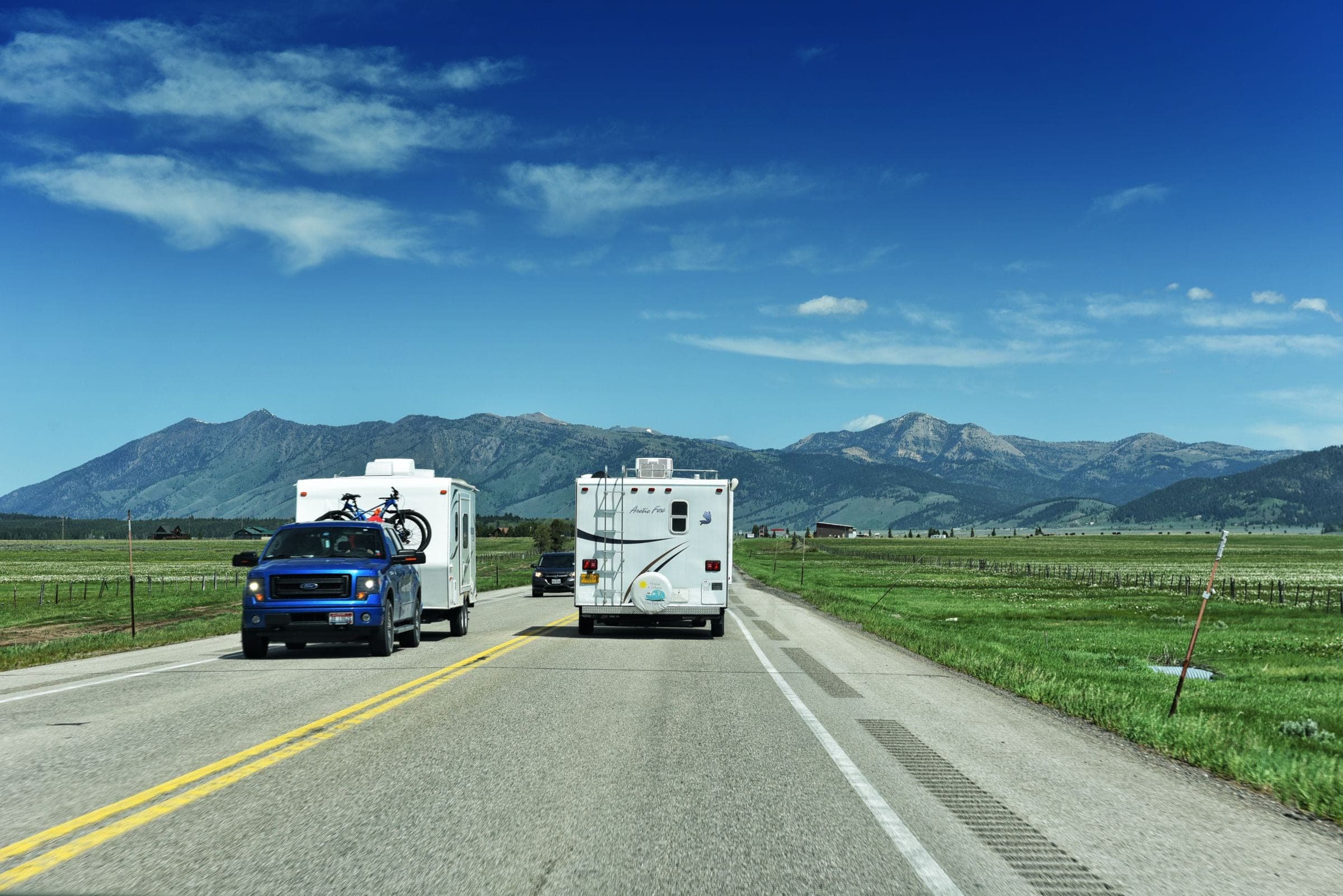 RV windshield replacement in Billings: pickup towing a camper and a motorhome on a Montana highway near the mountains