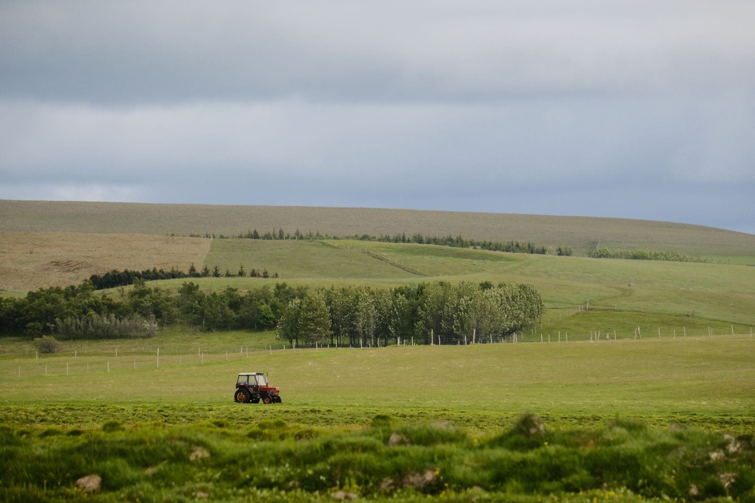 Windshield replacement for Huntley, MT drivers: red tractor working green farmland under a cloudy sky