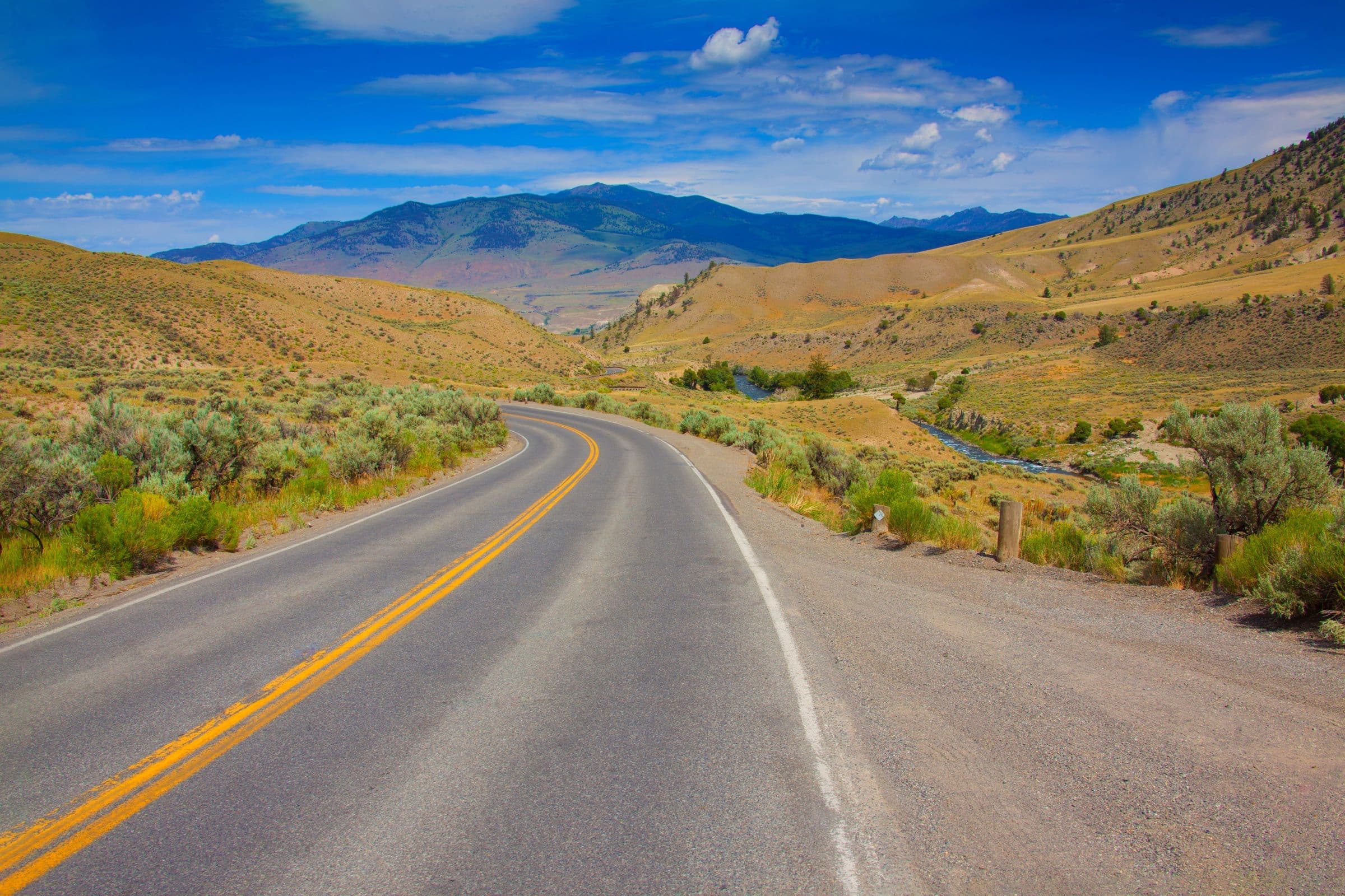 Windshield replacement for Park City, MT drivers: curving two-lane road through dry hills and mountains